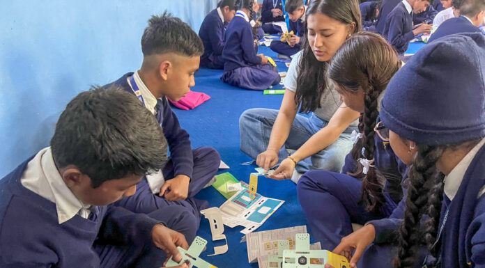 Mercer students bring innovative microscopes to schools in Nepal Students in uniforms sit on the floor, engaged in a collaborative educational activity with papers and small blocks.