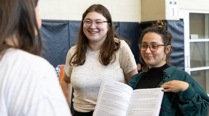 Mercer students receive Best Student Project Award at 2025 Gulf-South Summit Two people stand and smile while showing an open book to a third person in an indoor setting.