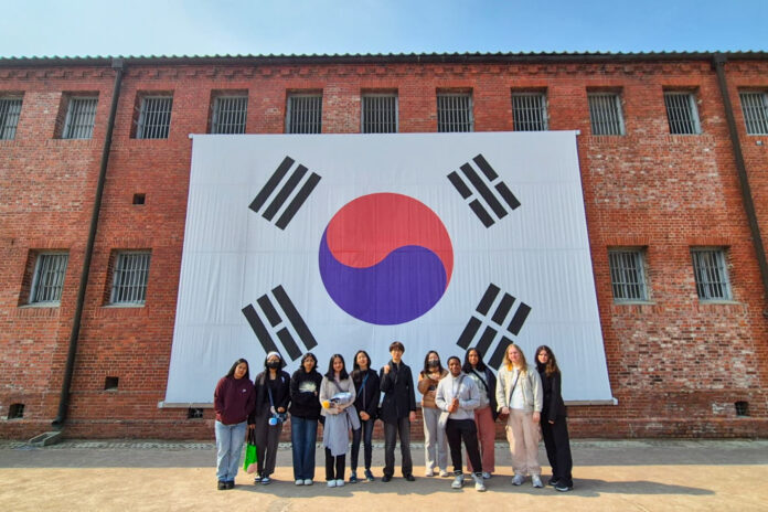 south-korea-3 A group of people stand in front of a large South Korean flag displayed on a brick wall.