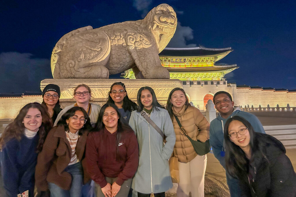 A group of people poses in front of the illuminated large stone statue at night.