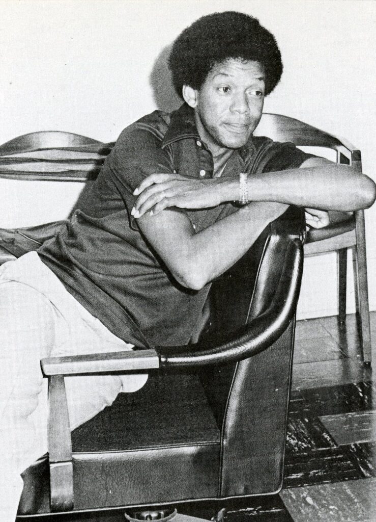 A person leans back in a chair with arms crossed, looking off to the side in a casual indoor setting.