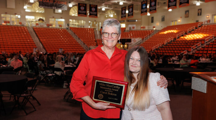 Pre-health advisor awarded Mike MacCarthy Mentorship Award Carol Bokros and Johna Wright stand together in an auditorium. Carol Bokros holds a plaque that reads Mike MacCarthy Membership Award.