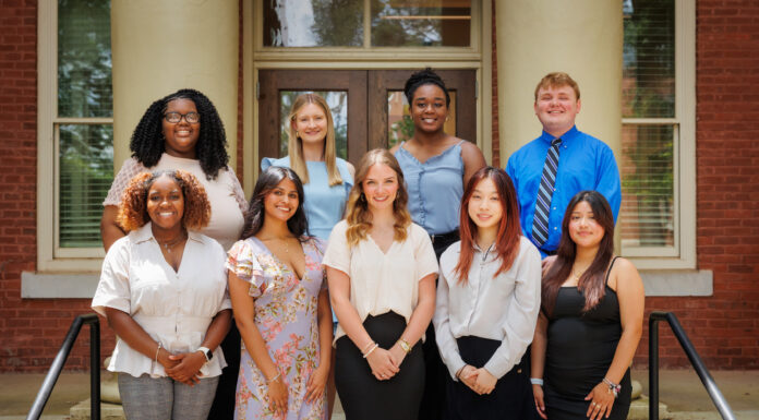 Seventeen students selected to study abroad as Gilman Scholars Nine people pose for a group photo on steps outside a brick building with white columns and glass doors.