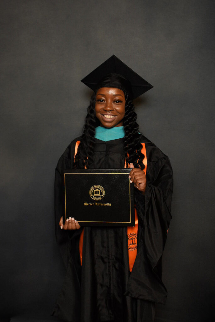 Aeeril Johnson in a graduation cap and gown holds a Mercer University diploma and smiles at the camera.