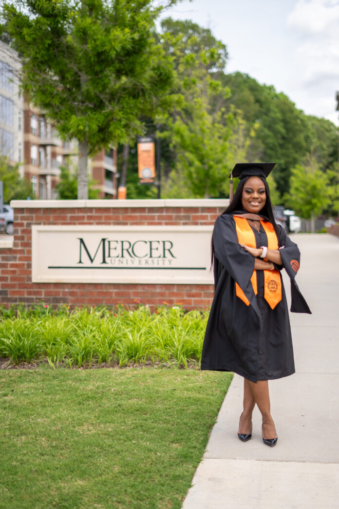 Anntoniette Walker, in cap and gown, stands smiling in front of a Mercer University sign.
