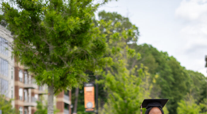Graduate Spotlight: Anntoniette Walker Anntoniette Walker, in cap and gown, stands smiling in front of a Mercer University sign.