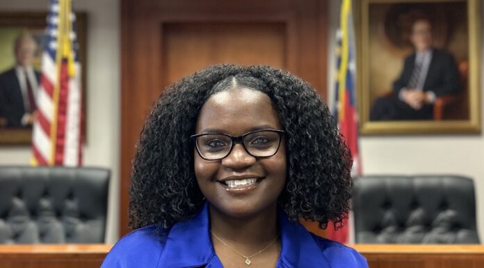 Rising senior Latoya Bartley named 2025 Phi Beta Kappa Key into Public Service scholar Woman in a blue blouse stands smiling in a courtroom with flags and framed portraits in the background.