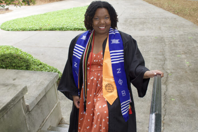 Bree Withrow, in graduation attire, stands on outdoor steps.