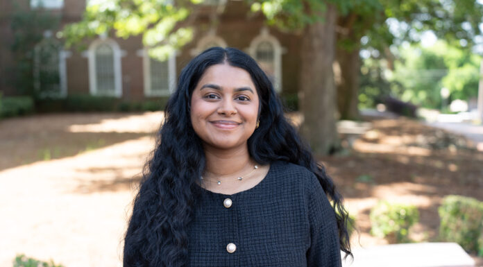 Mercer law student developing skills to be effective advocate Briana John stands outside, smiling, wearing a black textured top with gold buttons.