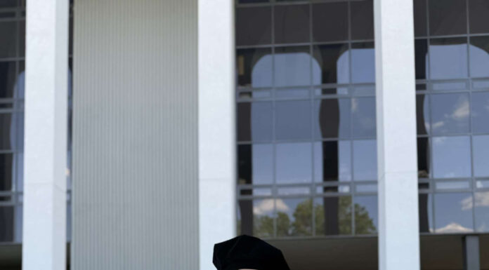 Graduate Spotlight: Glennessa Hodge Glennessa Hodge, in a cap and gown, stands smiling outside a modern building.
