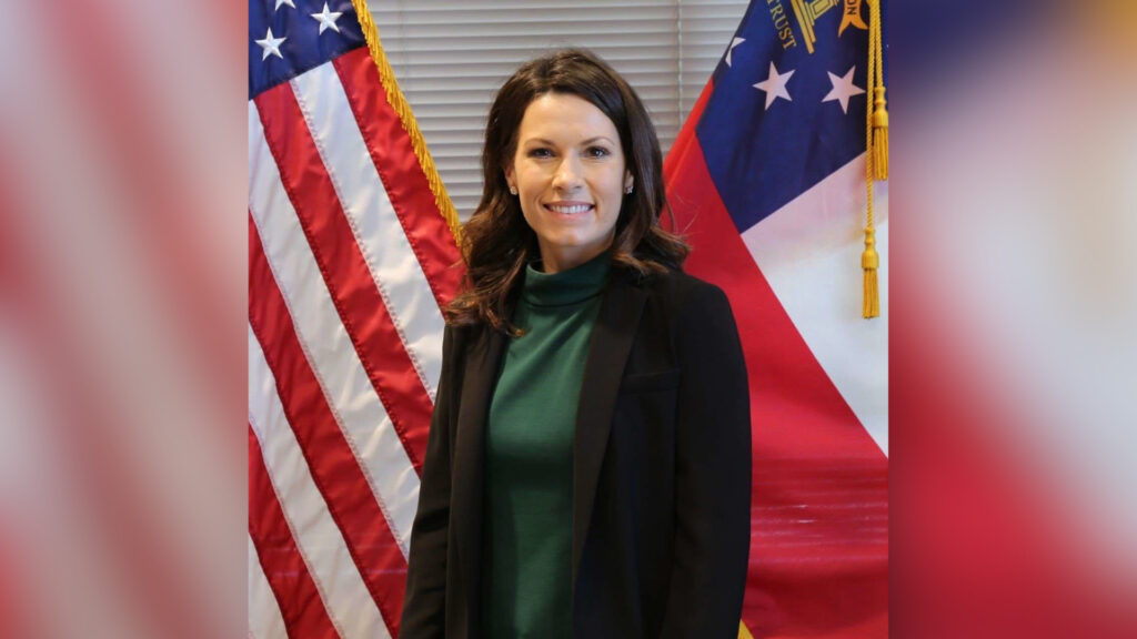 Woman standing in front of the American flag and the Georgia state flag, smiling at the camera.