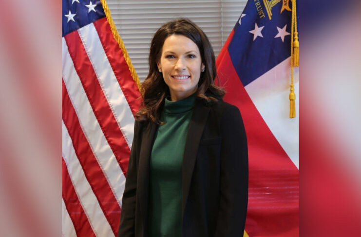 Woman standing in front of the American flag and the Georgia state flag, smiling at the camera.