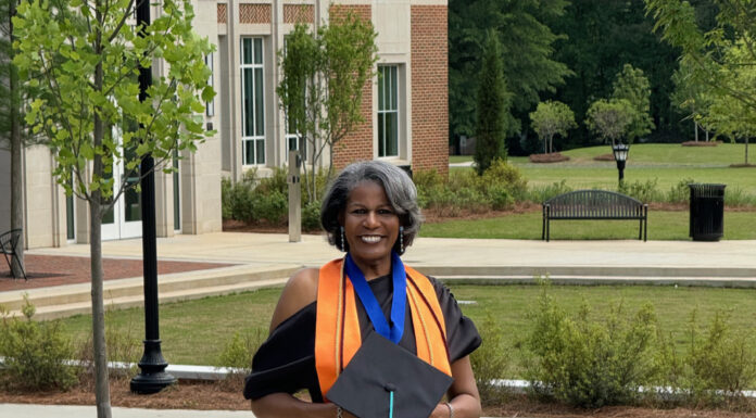 Graduate Spotlight: Leidra Dunson Leidra Dunson, in a graduation outfit, holds a cap and smiles while standing on a sidewalk near a building.