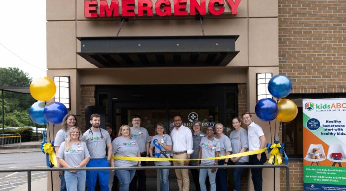 Kids Alliance for Better Care celebrates Monroe County Hospital emergency department as part of Pediatric Emergency Care Project A group of people stands in front of an emergency entrance for a ribbon-cutting ceremony with balloons and a banner.