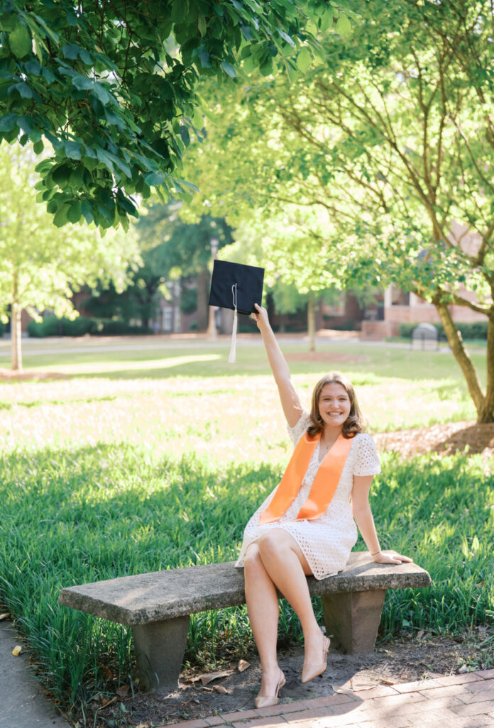 Maegan Ennis in a white dress and orange stole, holding up a graduation cap.