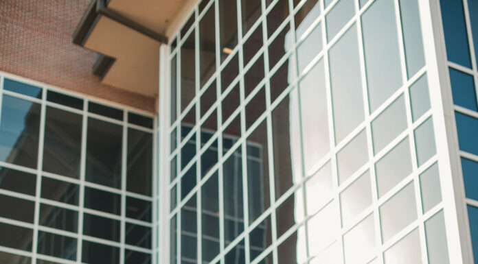 Graduate Spotlight: Maya Henry Maya Henry, in graduation attire, stands outside a modern glass building, smiling and posing for a photo.