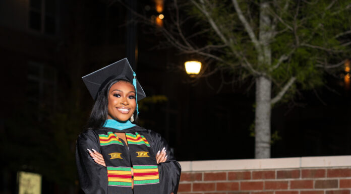 Graduate Spotlight: Morgan Taylor Morgan Taylor, in cap and gown, stands with arms crossed in front of a Mercer University sign at night.
