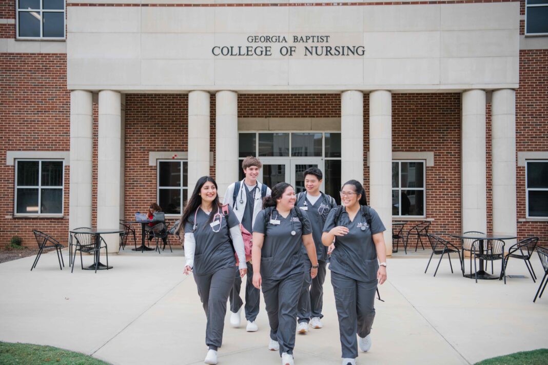Five nursing students in scrubs walk together outside the Georgia Baptist College of Nursing building.