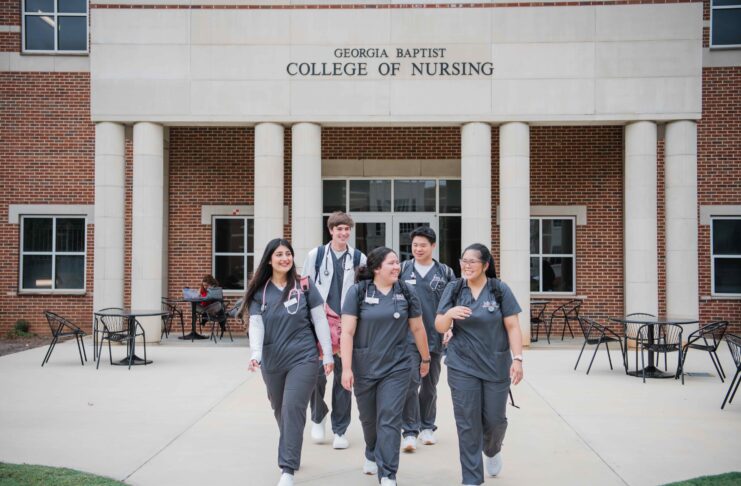 Five nursing students in scrubs walk together outside the Georgia Baptist College of Nursing building.