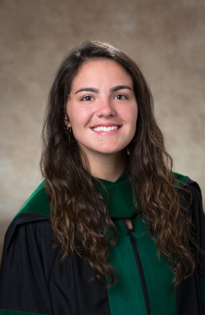 Susanna Jenkins, in a graduation gown and hood, poses for a formal studio portrait against a neutral background.