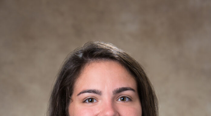 Graduate Spotlight: Susanna Jenkins Susanna Jenkins, in a graduation gown and hood, poses for a formal studio portrait against a neutral background.
