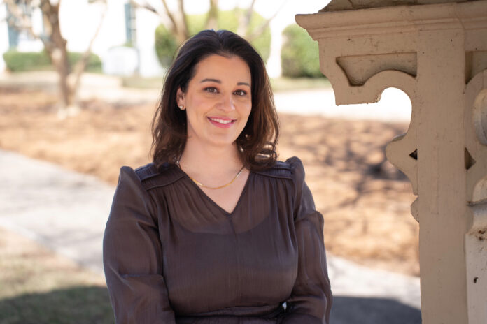 Elizabeth Nelms smiles while standing outdoors near a decorative wooden structure.