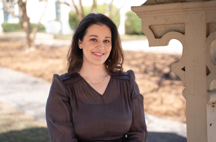 Elizabeth Nelms smiles while standing outdoors near a decorative wooden structure.