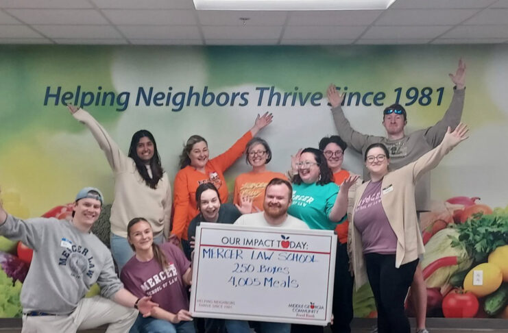 A group of people poses indoors, holding a sign that reads, Mercer Law School: 250 Boxes, 4,005 Meals.