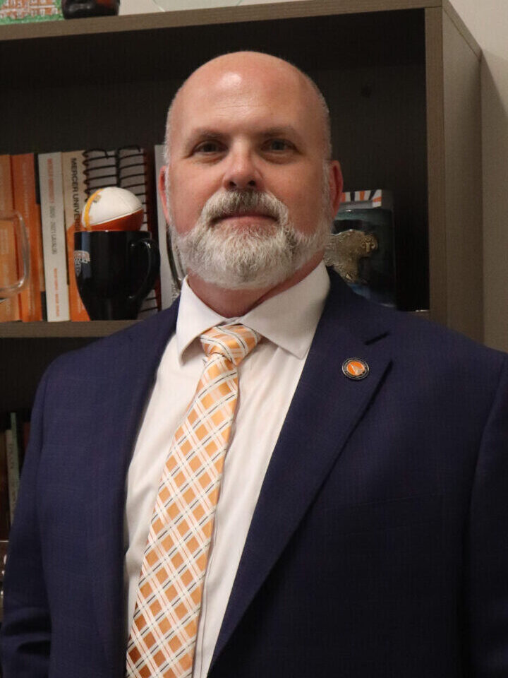 Garland Crawford, wearing a navy blue suit and orange checkered tie, stands in front of a book shelf.