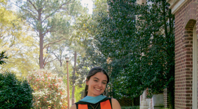 Graduate Spotlight: Morgan Goeckel Morgan Goeckel, in graduation attire, walks down a brick path outdoors, holding her cap and smiling.