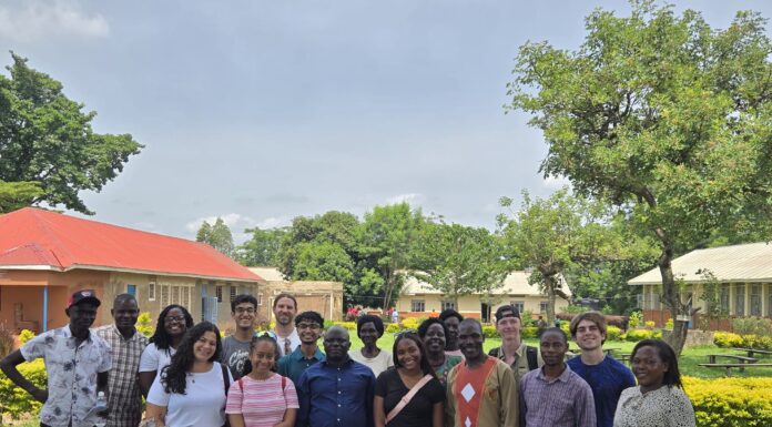 Mercer team leads nutrition, health workshops during Uganda trip A group of people stands together outdoors on grass, smiling, with buildings and trees in the background.