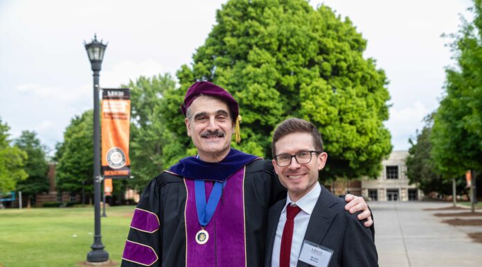 School of Business announces annual IAPP Westin Scholar Two men, one in academic regalia and one in a suit, stand together outside on a campus with green trees in the background.