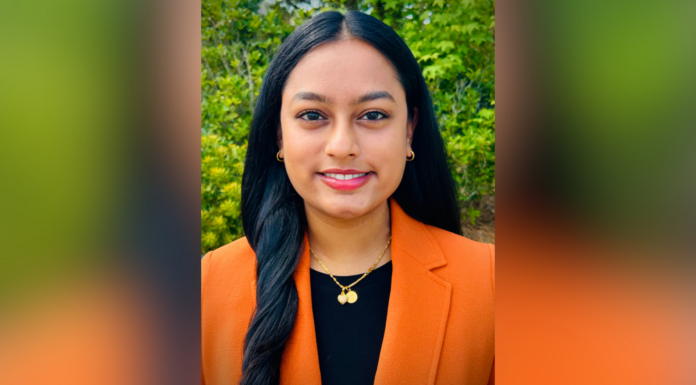 Engineering rising senior Cynthia Gaddam selected as Tau Beta Pi scholar A woman with long dark hair in an orange blazer stands outdoors, smiling slightly, with greenery in the background.
