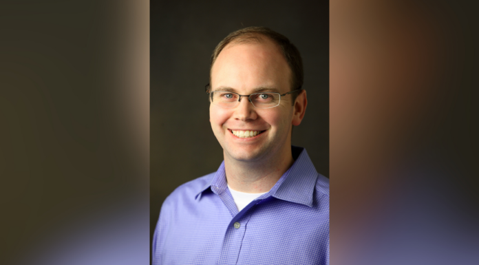 Dr. David Goode appointed associate dean of College of Liberal Arts and Sciences Man with glasses and short hair wearing a light purple collared shirt, smiling in front of a dark background.
