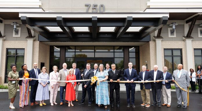 A group of Mercer University representatives as well as state and local Georgia officials stand in front of a building holding a large ribbon at a ribbon-cutting ceremony.