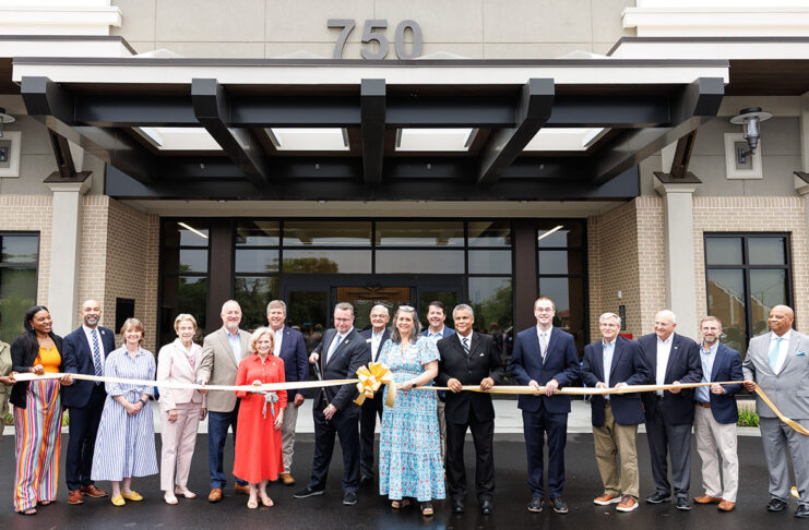 A group of Mercer University representatives as well as state and local Georgia officials stand in front of a building holding a large ribbon at a ribbon-cutting ceremony.