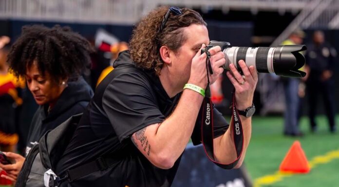 Mercer alumnus proud to tell Bibb County School District stories A photographer takes pictures on a sports field with a Canon camera and telephoto lens.
