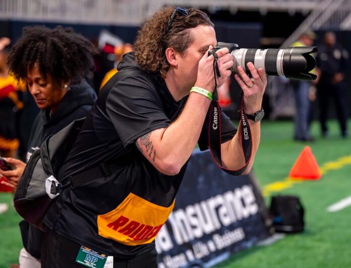 Jeremy photo by Michael Woody A photographer takes pictures on a sports field with a Canon camera and telephoto lens.