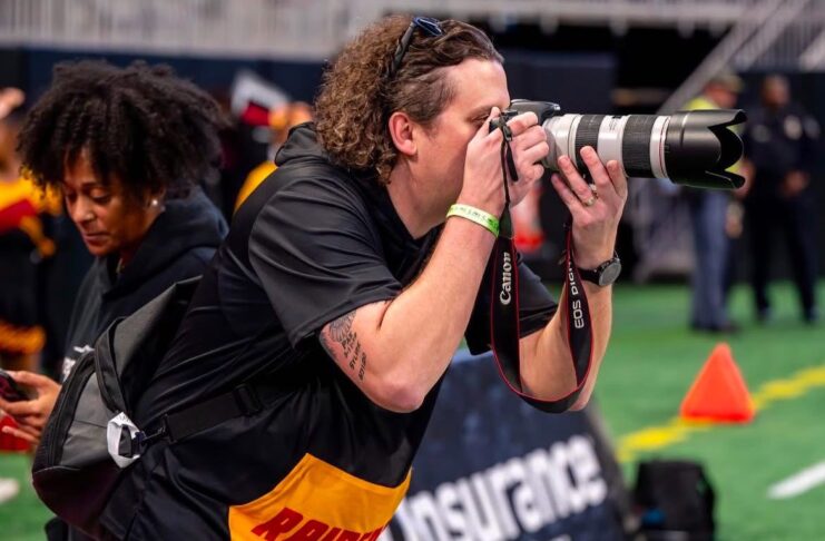 A photographer takes pictures on a sports field with a Canon camera and telephoto lens.