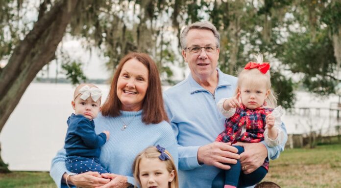 Alumna dedicated to serving the community of Sebring, Florida Two adults and four young children pose for a family photo outdoors on grass with trees and water in the background.