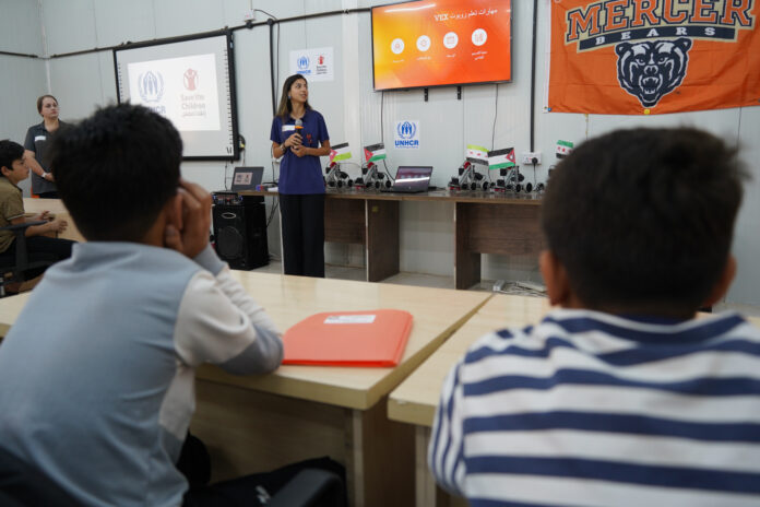 mom-jordan-3 A woman presents to a classroom of students with UNHCR and Save the Children logos displayed on the screen.
