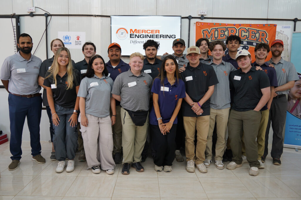 Group of students and adults pose indoors in front of Mercer Engineering banners, smiling at the camera.
