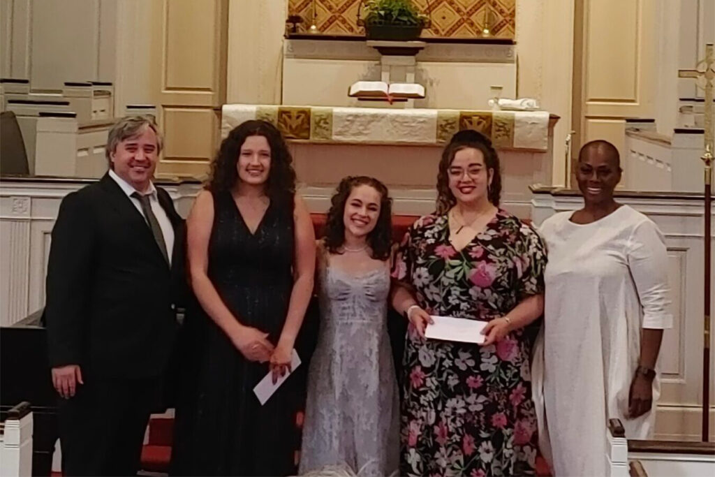 Five people stand at the front of a church sanctuary, posing for a group photo near the altar.