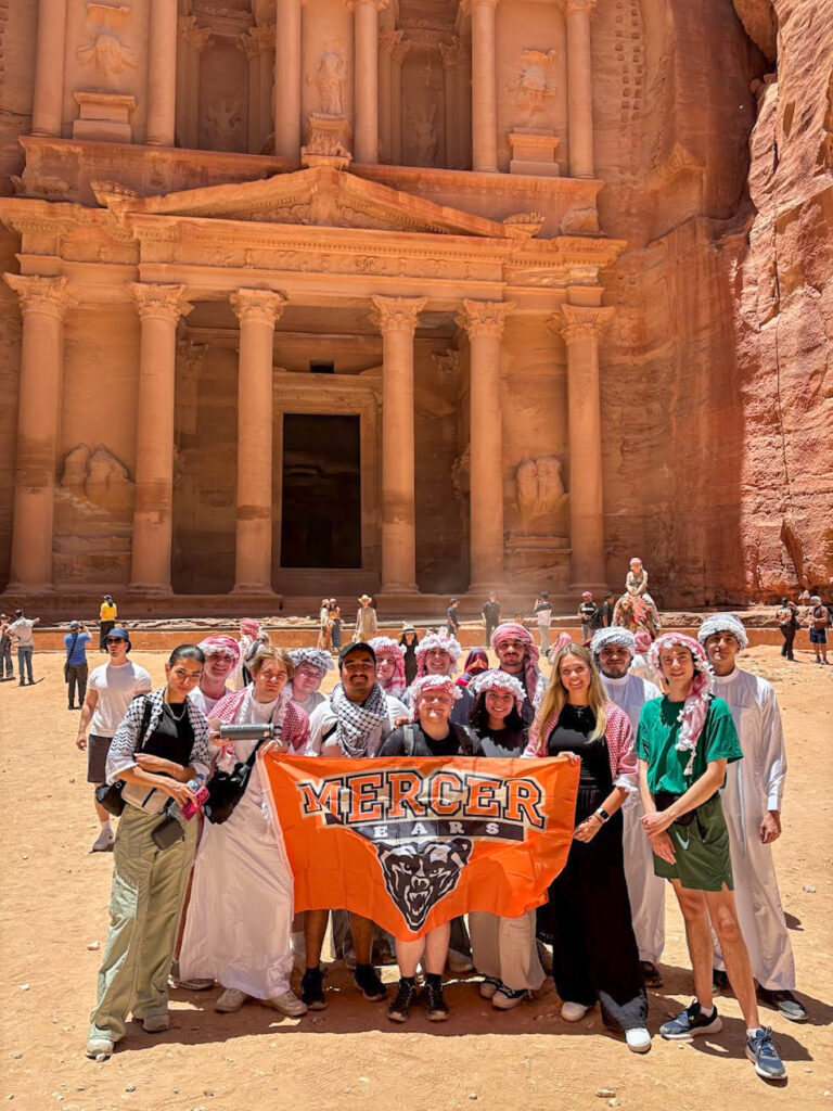 A group of people hold a Mercer Bears banner in front of the ancient Al-Khazneh structure in Petra, Jordan.