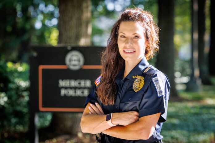 A Mercer Police Chief Haley Beckham stands outdoors with arms crossed, smiling in front of a Mercer Police sign.