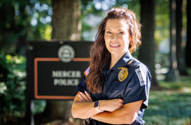 A Mercer Police Chief Haley Beckham stands outdoors with arms crossed, smiling in front of a Mercer Police sign.