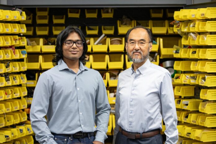 Two men standing in front of shelves with yellow storage bins filled with various items, both looking at the camera.