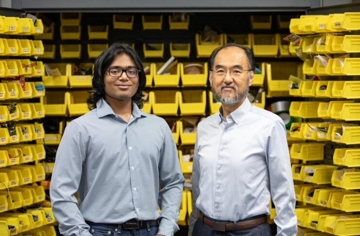 Two men standing in front of shelves with yellow storage bins filled with various items, both looking at the camera.