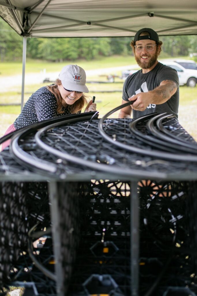 Two people assemble a large black plastic structure outdoors under a canopy.