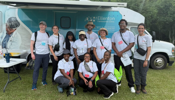 fwfhp 2025 A group of people in matching shirts pose in front of a mobile health clinic parked on grass.